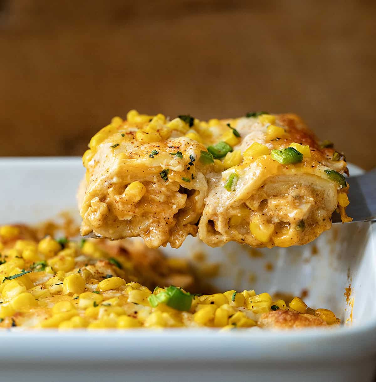 Spatula picking up two Street Corn Chicken Enchiladas from the pan.