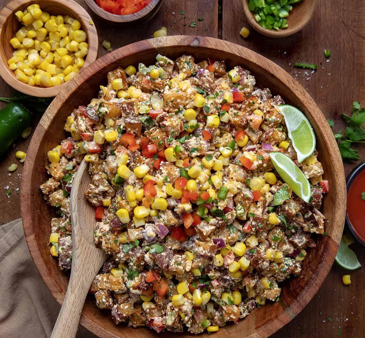 If you love my super popular Roasted Potato Salad that everyone asks for (the original and the best!), you will love this Street Corn Roasted Potato Salad, too! This version builds on everything you already love like crispy roasted potatoes, zesty dressing, and fresh vegetables, but it adds a vibrant mix of corn, jalapeño, and cotija cheese that takes it to the next level! Wooden bowl filled with Street Corn Roasted Potato Salad with a wooden spoon in it.
