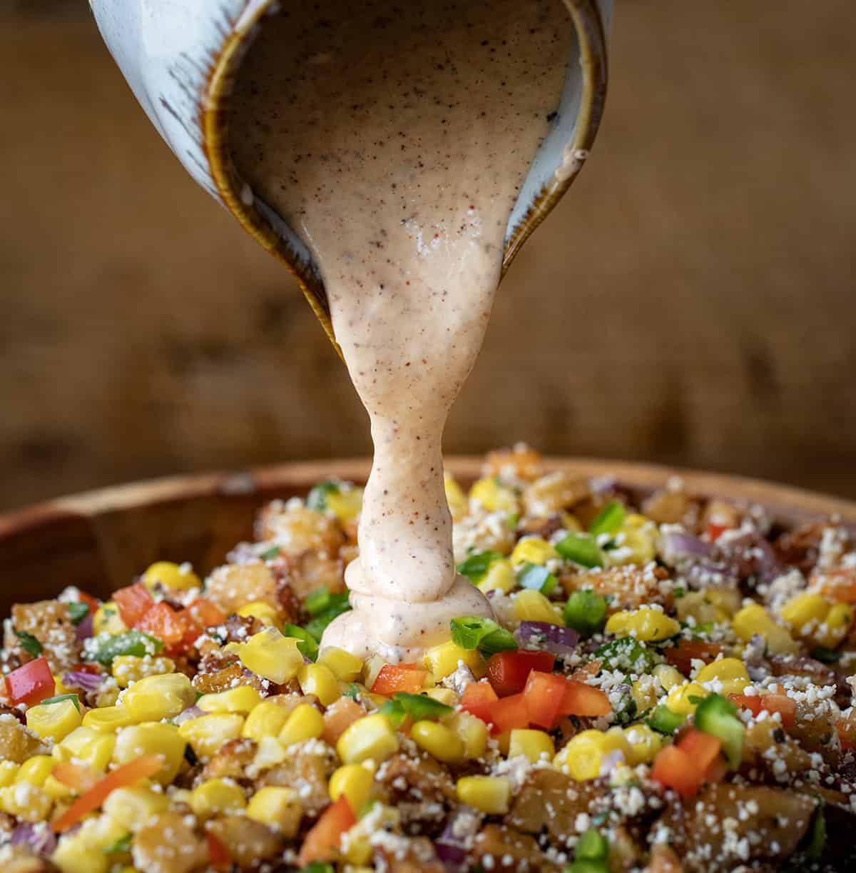 Pouring dressing over Street Corn Roasted Potato Salad.