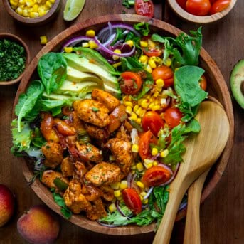 Bowl of Sweet and Spicy Chicken Peach Salad with wooden salad spoons in it from overhead.