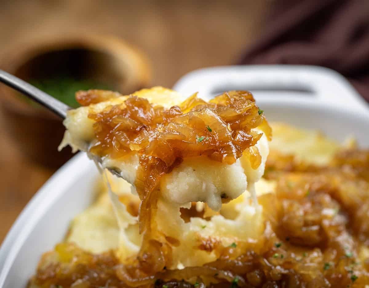 Spoonful of Twice Baked French Onion Mashed Potatoes being held above the pan.