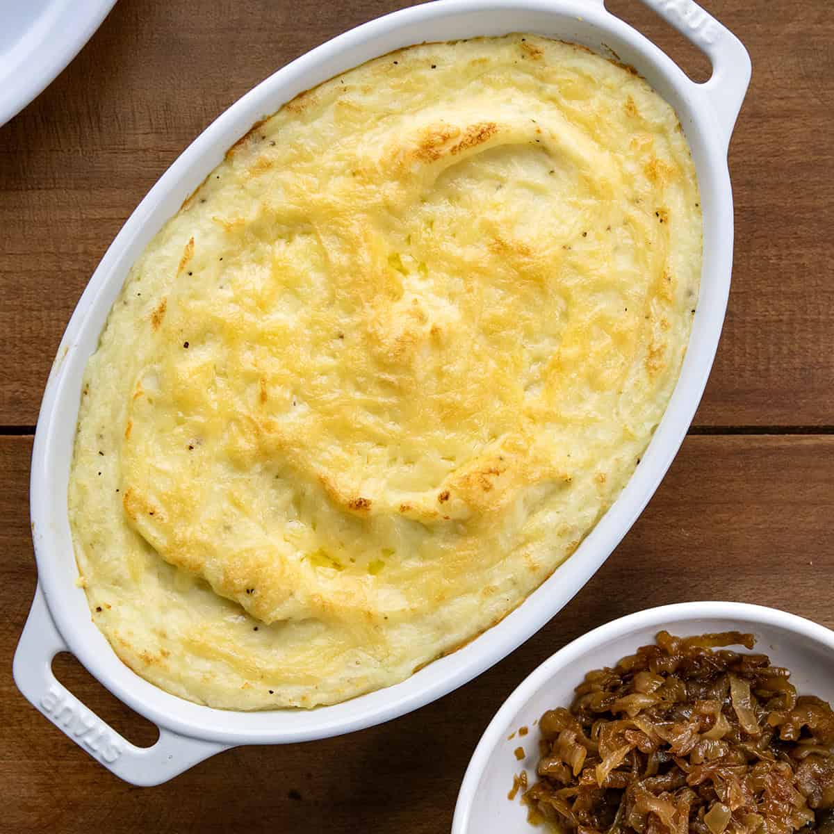 Twice-baked potatoes in a pan next to a plate of caramelized onions on a wooden table from overhead.