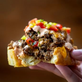 Hand holding a piece of Cheeseburger Garlic Bread.