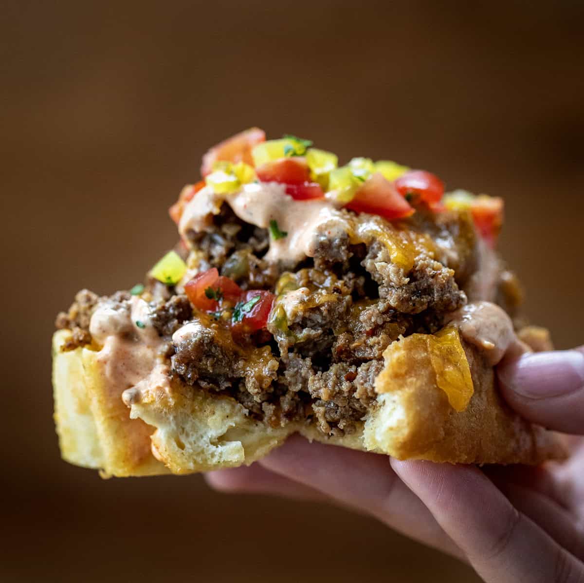 Hand holding a piece of Cheeseburger Garlic Bread.