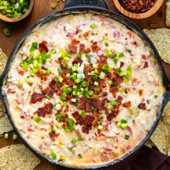 Skillet of Chicken Bacon Ranch Queso on a wooden table with tortilla chips from overhead.