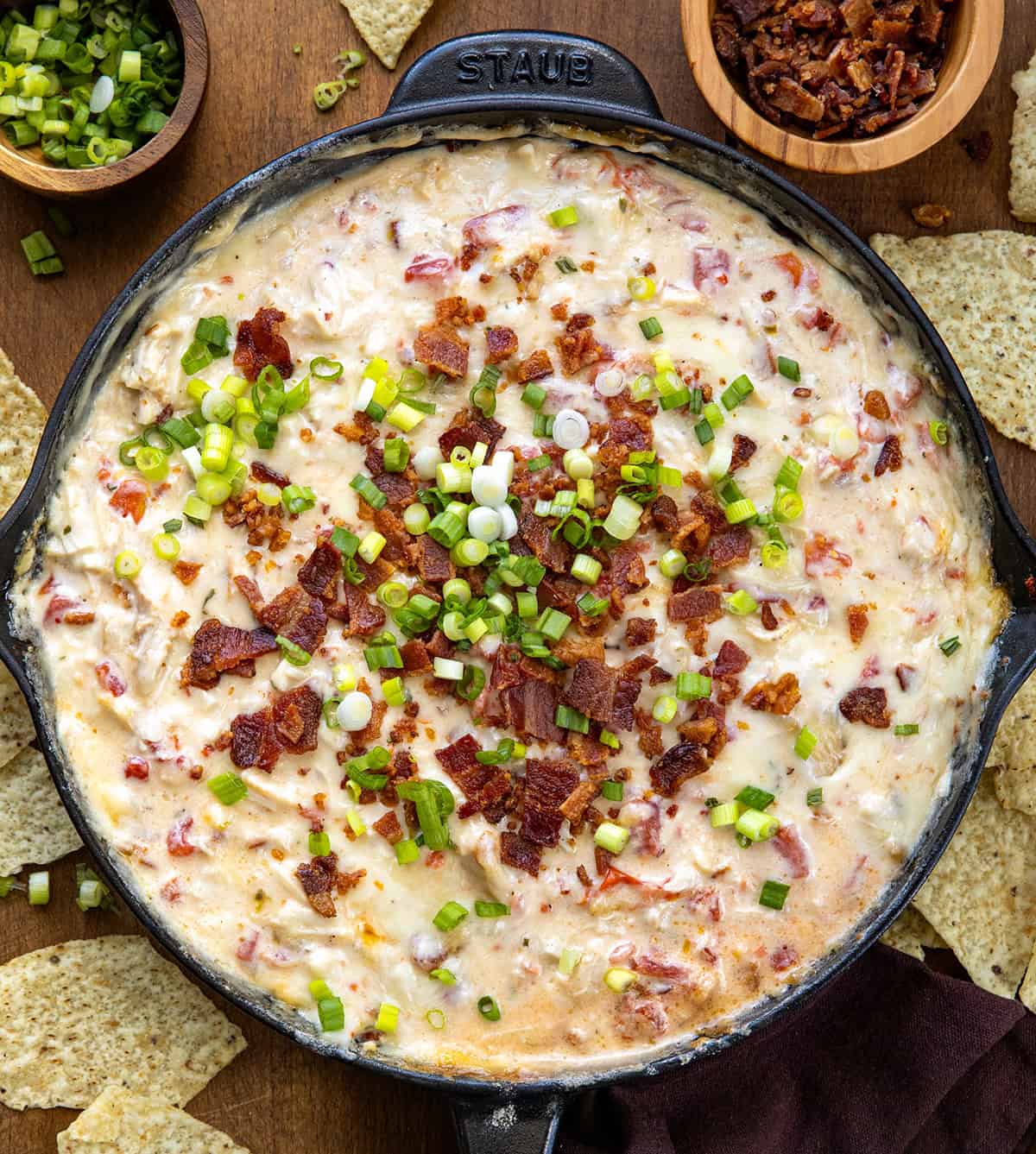 Skillet of Chicken Bacon Ranch Queso on a wooden table with tortilla chips from overhead.