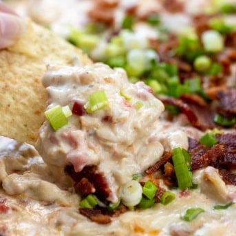 Chip scooping up creamy Chicken Bacon Ranch Queso from the skillet close up.