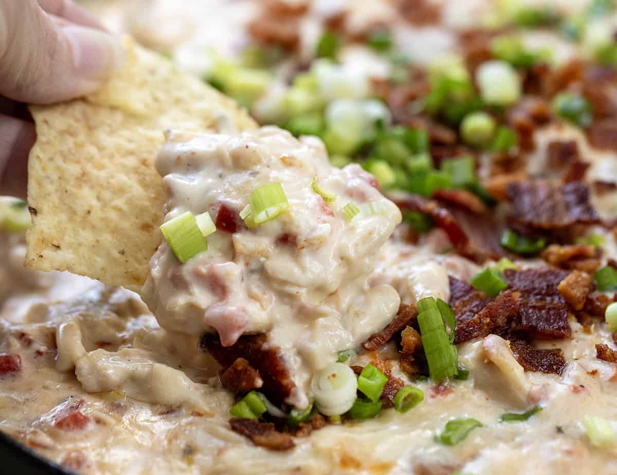 Chip scooping up creamy Chicken Bacon Ranch Queso from the skillet close up.
