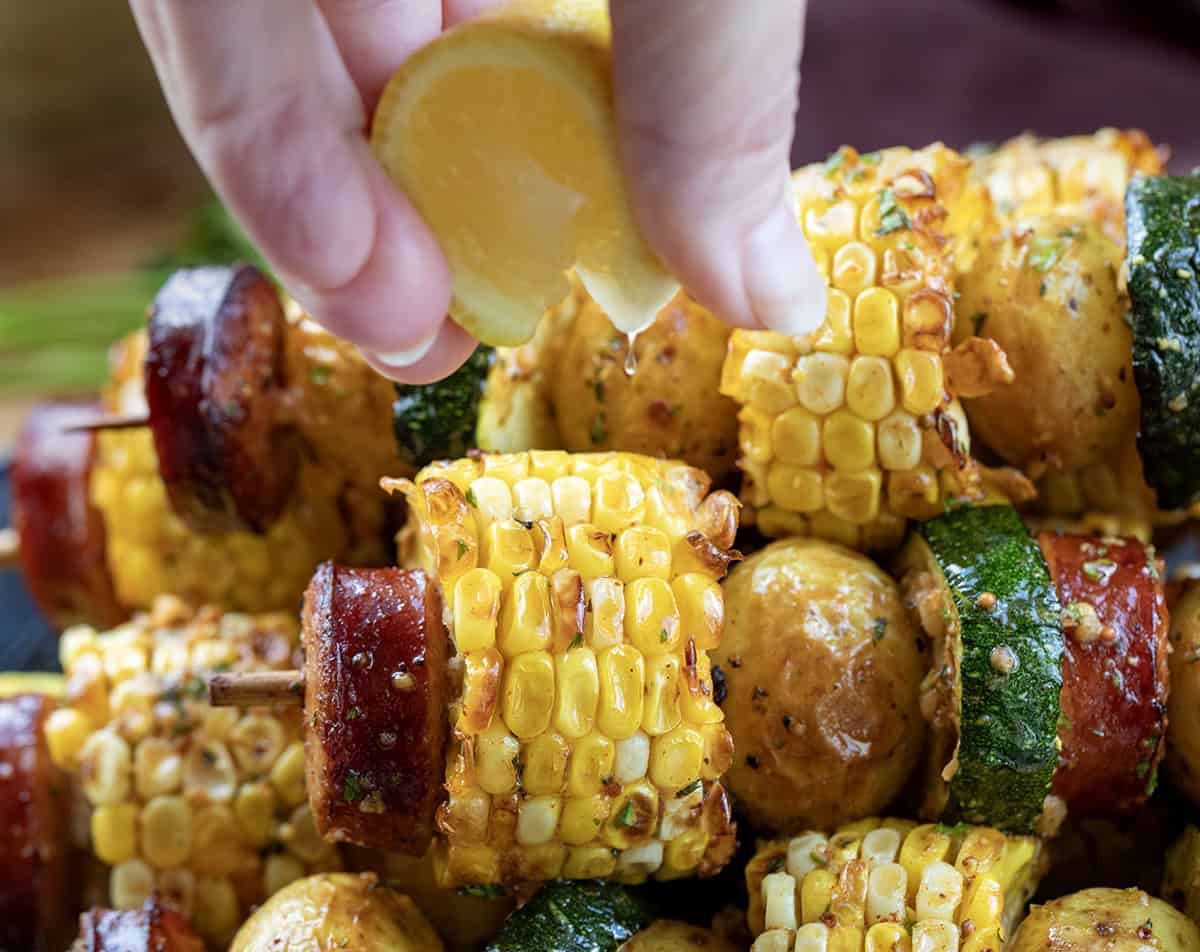 Hand squeezing lemon over Cowboy Butter Kielbasa and Potato Skewers.