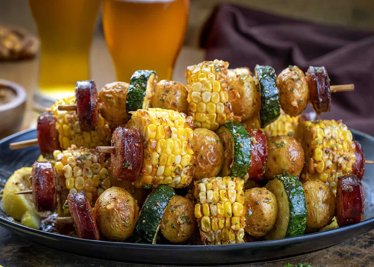 Platter of Cowboy Butter Kielbasa and Potato Skewers with beer in the background.