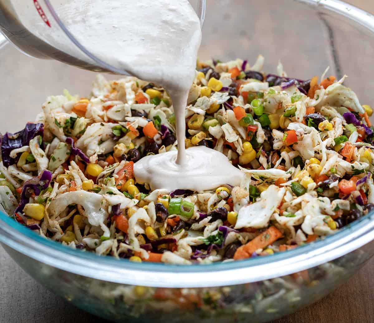 Pouring dressing over Cowboy Cabbage in a glass bowl before fritos are added.