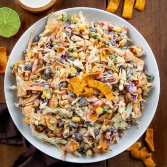 White bowl filled with Cowboy Cabbage on a wooden table surrounded by fritos.