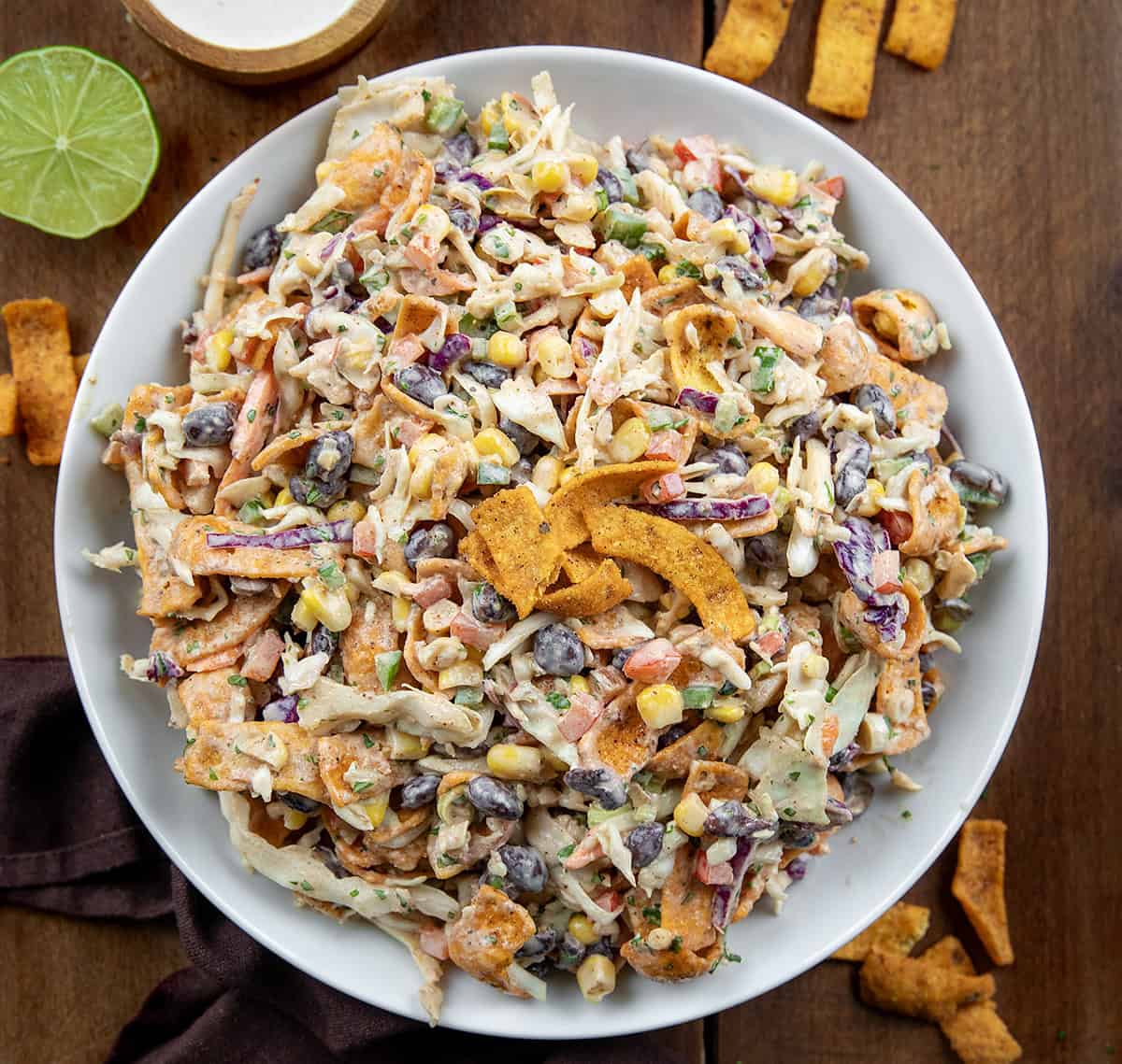 White bowl filled with Cowboy Cabbage on a wooden table surrounded by fritos. 
