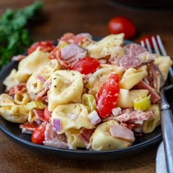 Black plate with Italian Grinder Tortellini Salad on it and a fork resting on the plate.