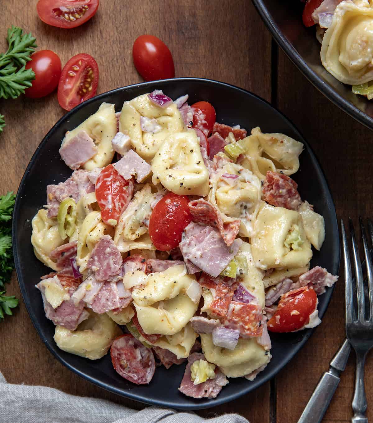 Black plate with Italian Grinder Tortellini Salad on it on a wooden table from overhead.