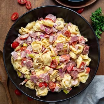 Black bowl of Italian Grinder Tortellini Salad on a wooden table from overhead.