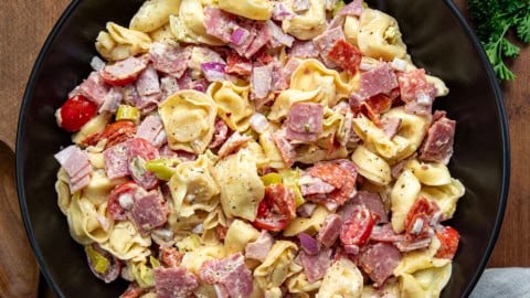 Black bowl of Italian Grinder Tortellini Salad on a wooden table from overhead.