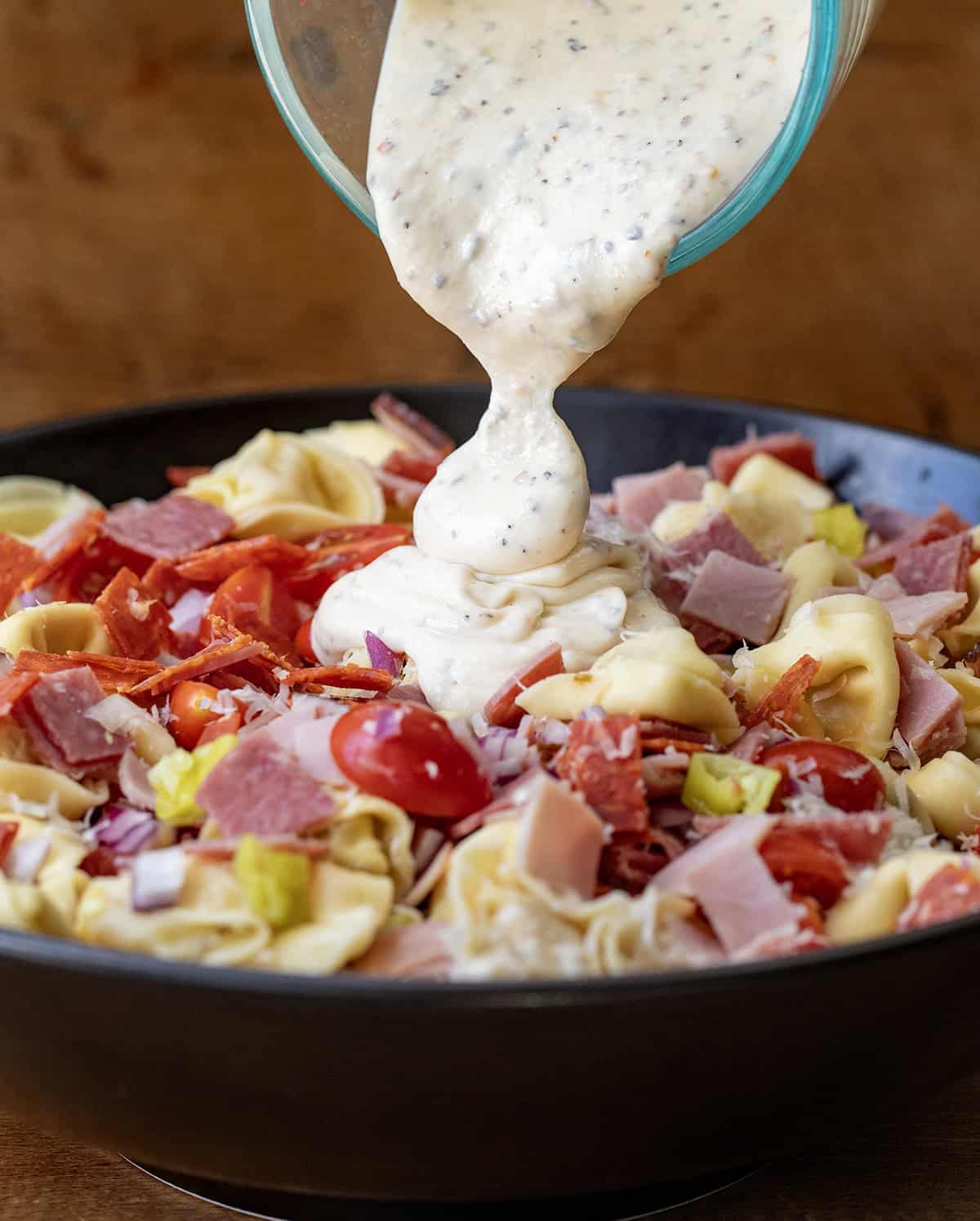 Pouring dressing on Italian Grinder Tortellini Salad.