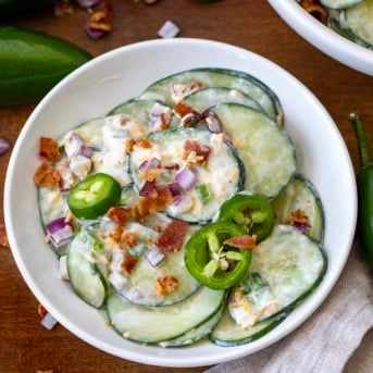White bowl of Jalapeno Popper Cucumber Salad on a wooden table.