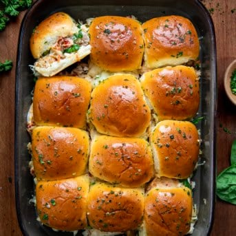 Marry Me Chicken Sliders in a pan with one slider on its side and sitting on a wooden table.