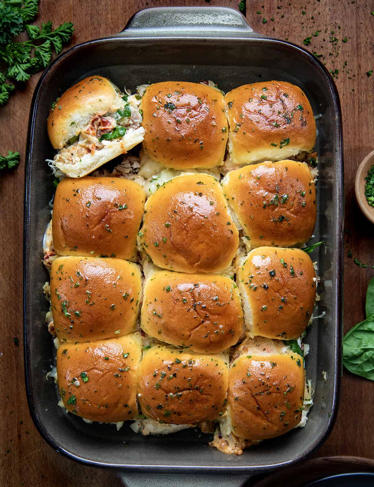 Marry Me Chicken Sliders in a pan with one slider on its side and sitting on a wooden table.