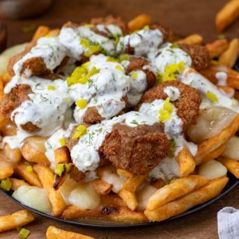 Skillet of Pickle Poutine on a wooden table with french fries and chopped pickles.