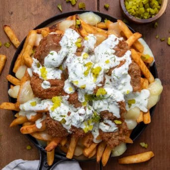 Skillet of Pickle Poutine on a wooden table with french fries and chopped pickles.