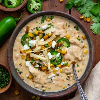 Bowl of Street Corn White Chicken Chili with a spoon in it on a wooden table from overhead.