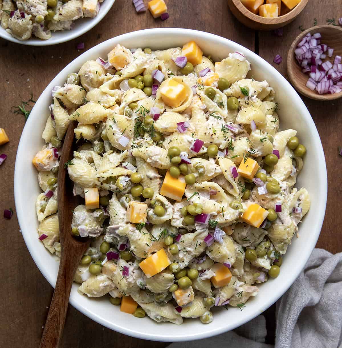 Looking for a delicious and easy cold pasta salad that’s perfect for lunch, potlucks, or a make-ahead dinner? This is becoming one of my go-to Tuna Pasta Salad recipes, and it always disappears fast. It starts with tender shell pasta, flaky tuna, sweet peas, and Colby Jack cheese, all tossed in a tangy, creamy pasta salad dressing Big white bowl of Tuna Pasta Salad on a wooden table from overhead.