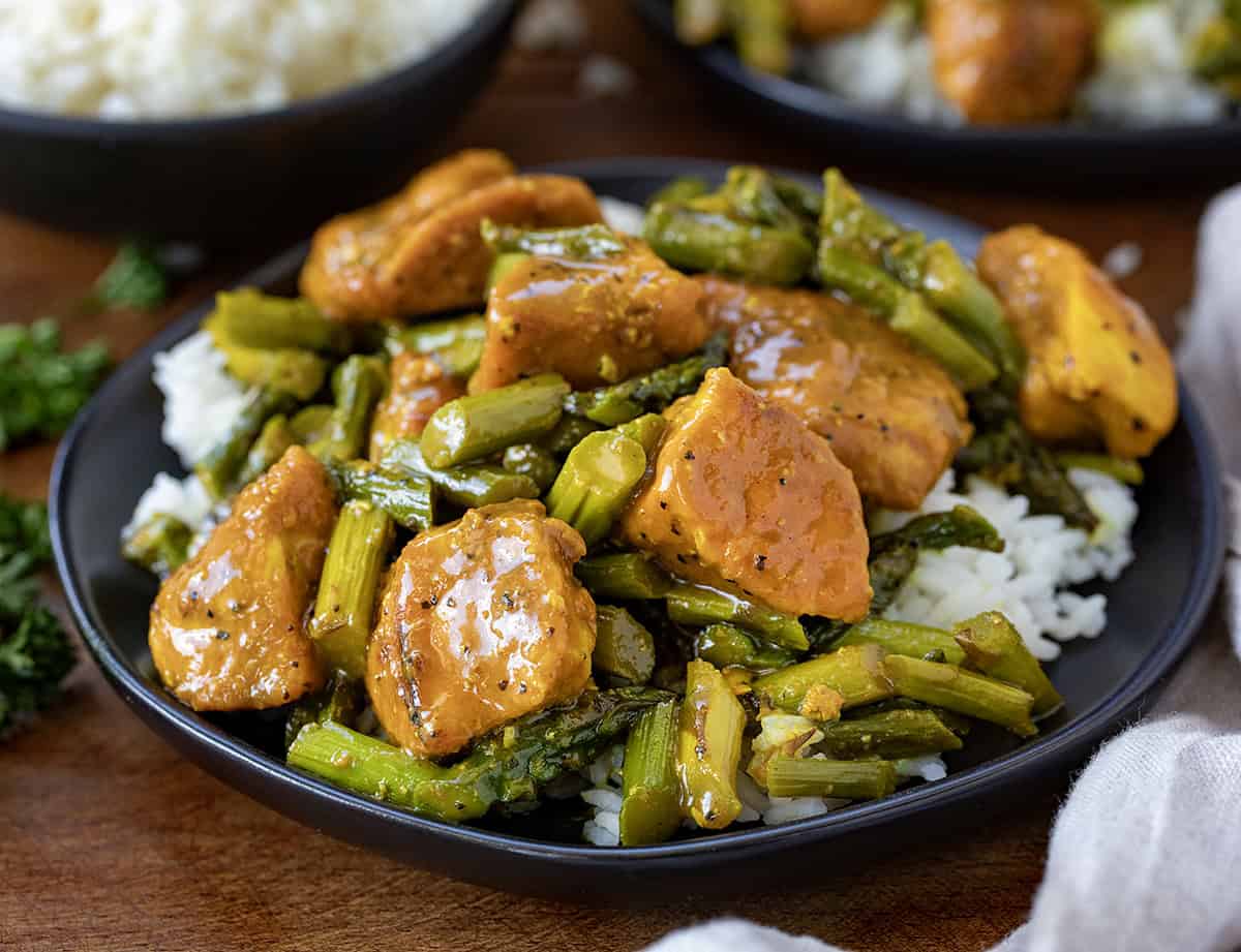 Black plate of Turmeric Black Pepper Chicken with Asparagus on a wooden table close up.