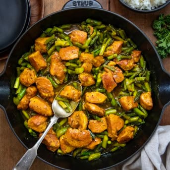 Skillet of Turmeric Black Pepper Chicken with a spoon in the skillet on a wooden table.