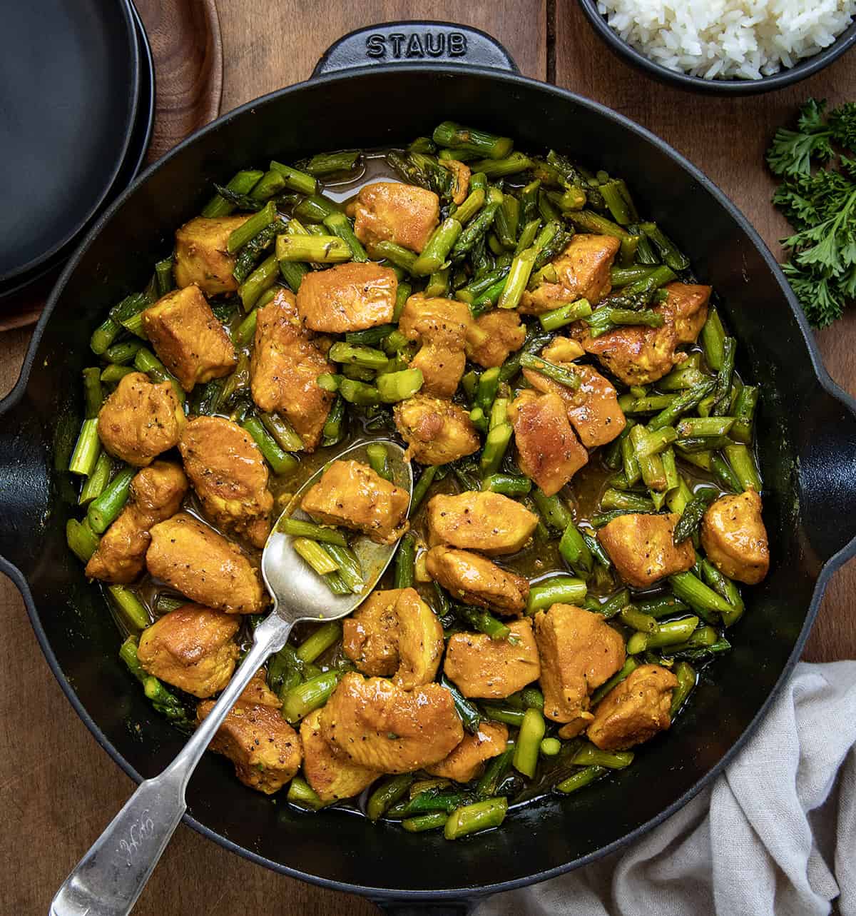 Make weeknight dinners simpler with Turmeric Black Pepper Chicken with Asparagus, a tasty dish ready in under 30 minutes, all in one skillet! Skillet of Turmeric Black Pepper Chicken with a spoon in the skillet on a wooden table.