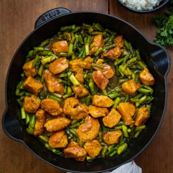 Black skillet of Turmeric Black Pepper Chicken on a wooden table from overhead.