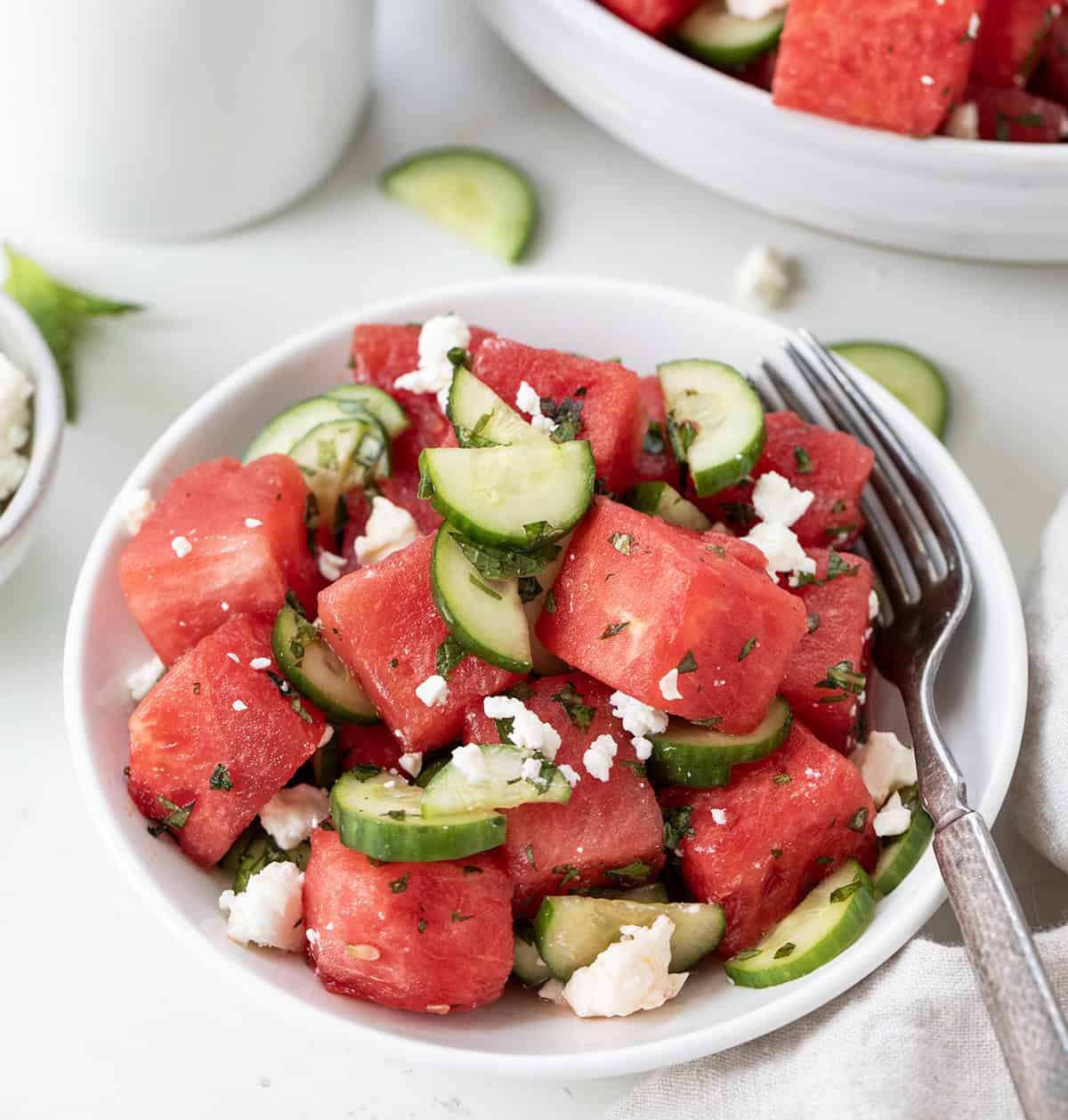 Small white plate with Watermelon Feta Salad and a fork on a white table.