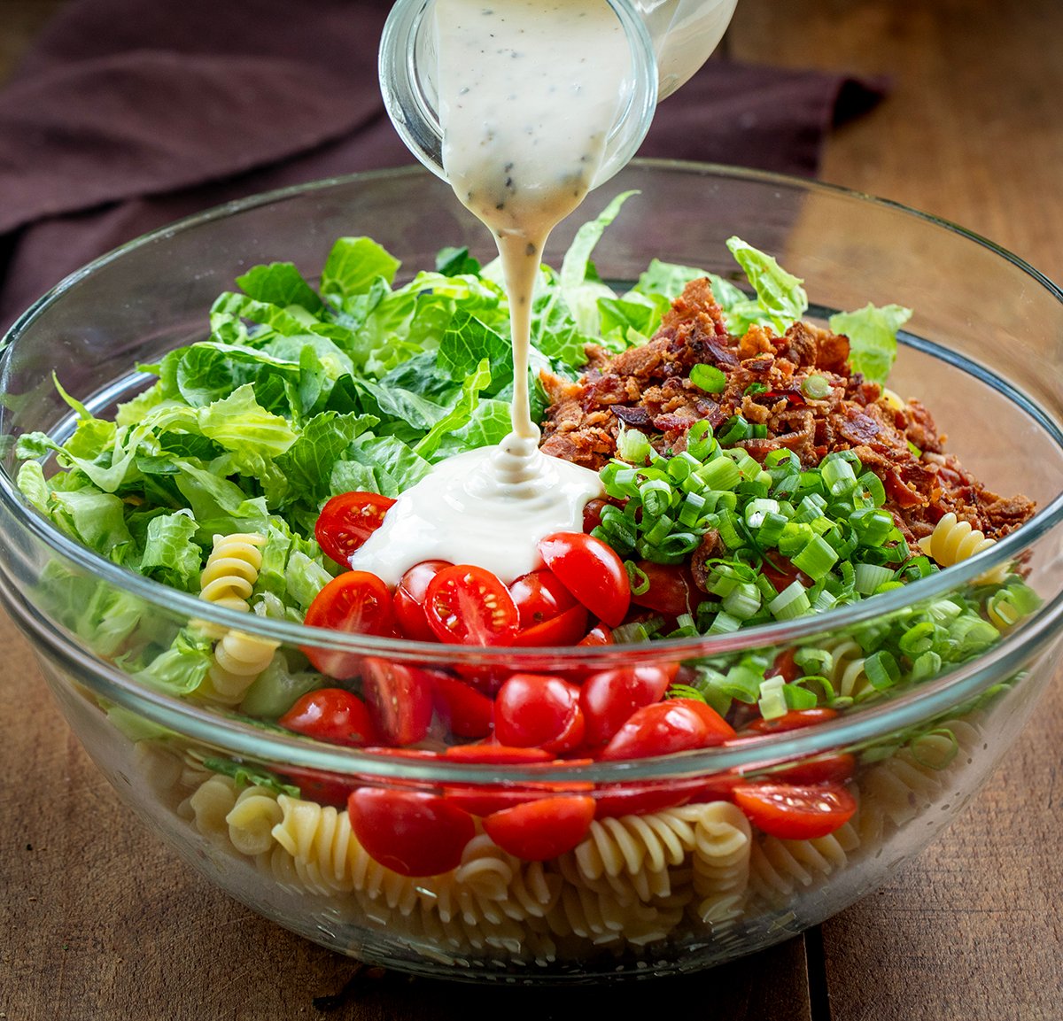 Pouring dressing over raw ingredients for BLT Pasta Salad.
