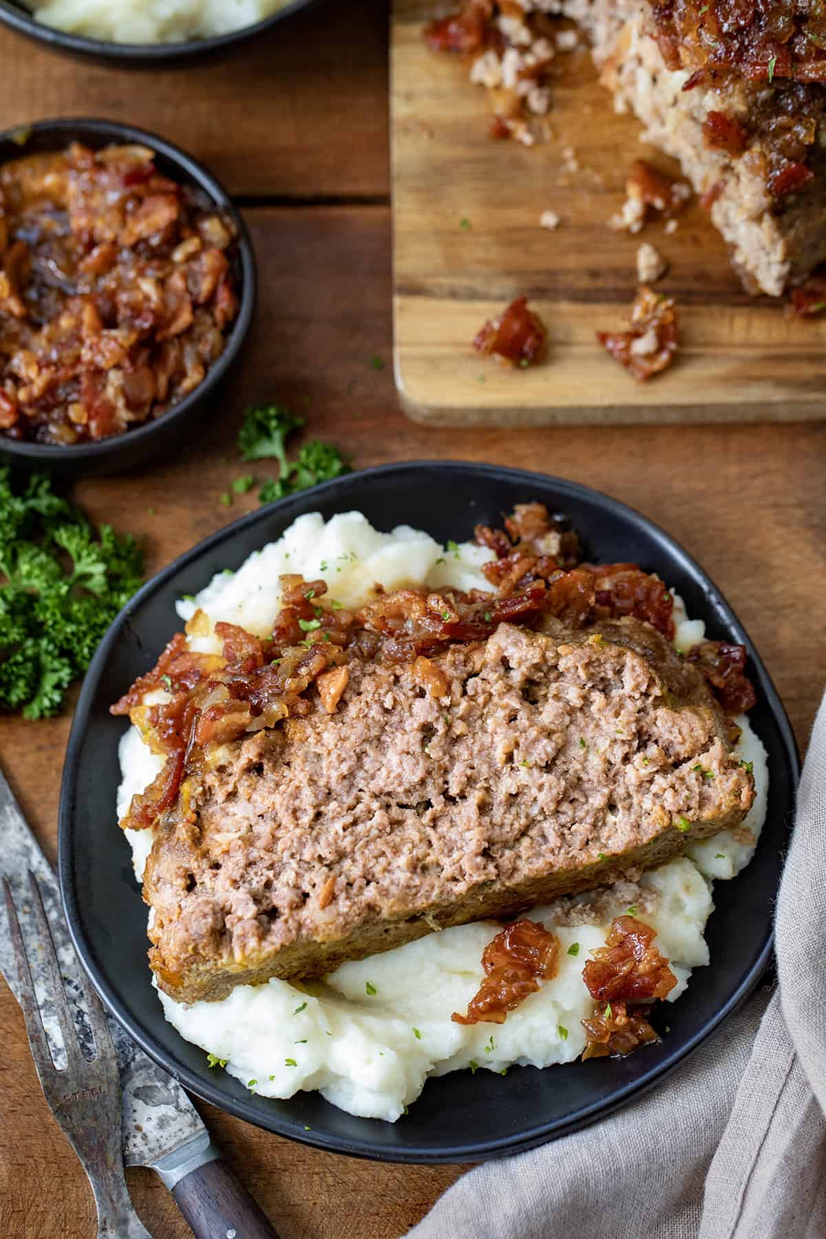 Slice of Bacon Jam Meatloaf on a bed of mashed potatoes on a black plate.