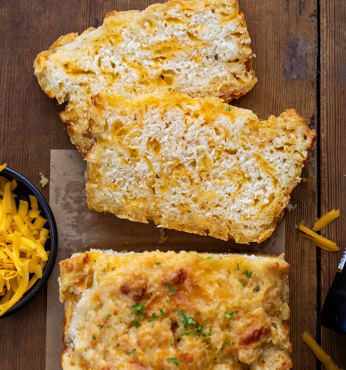 Loaf of Beer Cheese Bread with a few pieces cut and laying flat on a wooden table from overhead.
