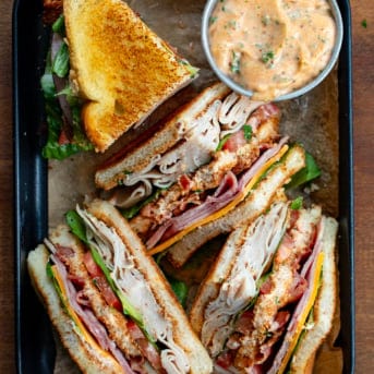 Quartered Cowboy Club Sandwiches on a tray with a bowl of cowboy mayo.