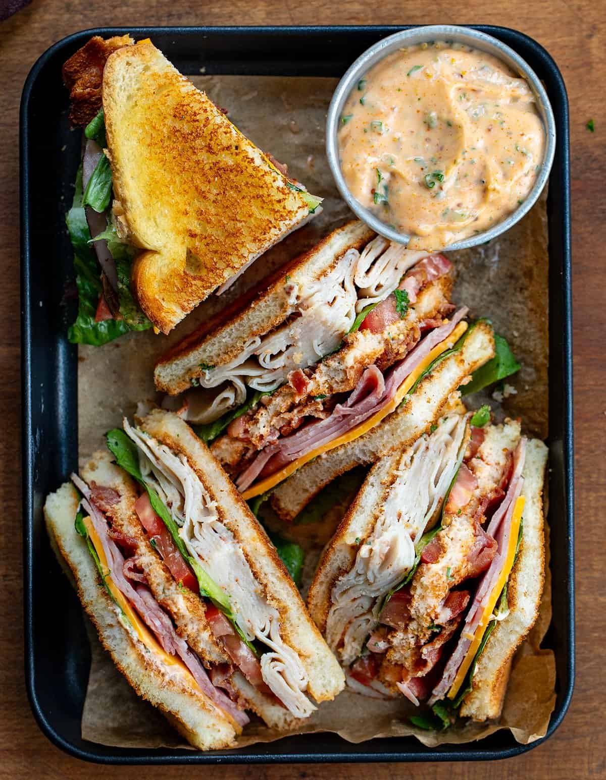Quartered Cowboy Club Sandwiches on a tray with a bowl of cowboy mayo.