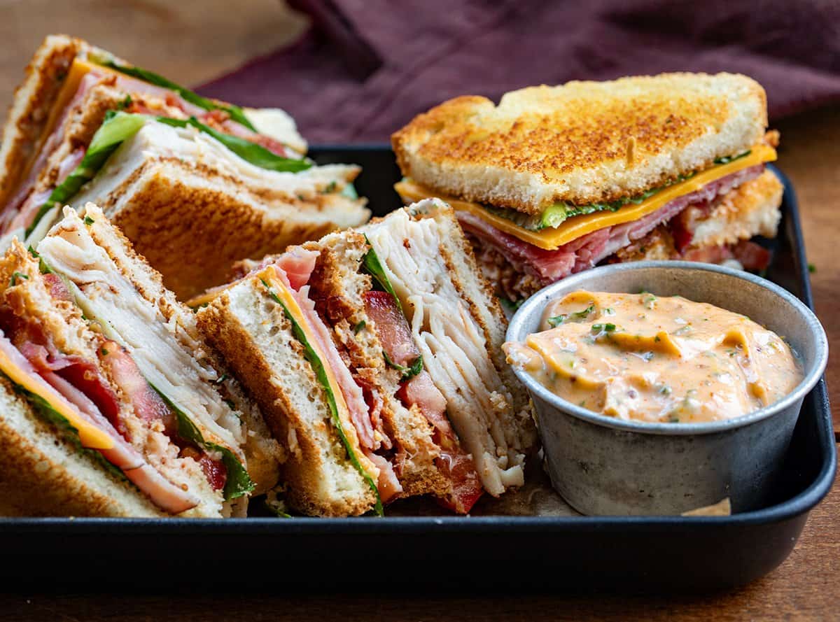 Quartered Cowboy Club Sandwiches on a tray with a bowl of cowboy mayo.