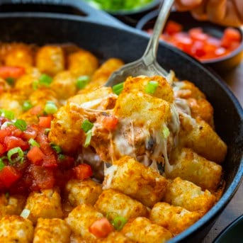 Spoon picking up a portion of Fiesta Chicken Tater Tot Casserole from the skillet.