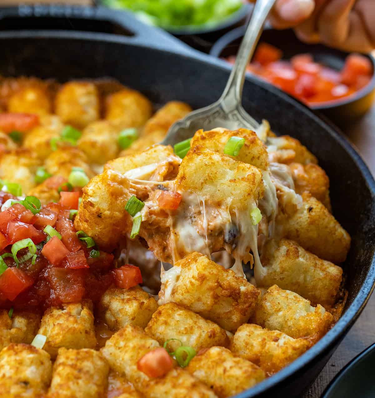 Spoon picking up a portion of Fiesta Chicken Tater Tot Casserole from the skillet.