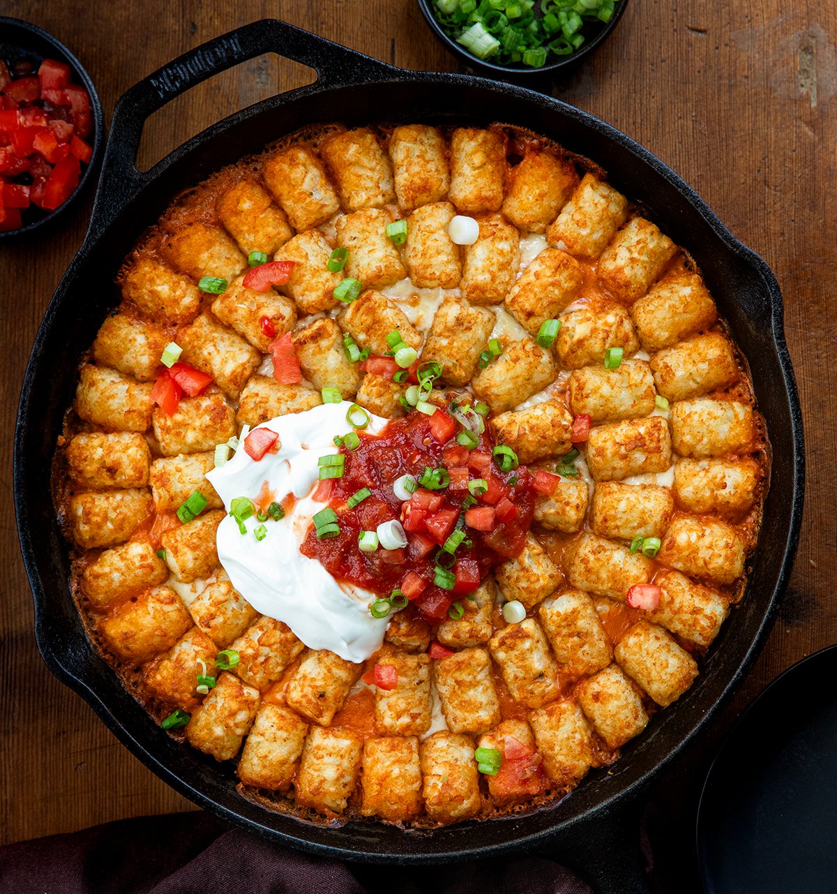 Skillet of Fiesta Chicken Tater Tot Casserole on a wooden table from overhead.