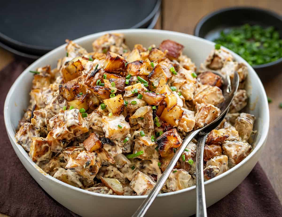 Bowl of French Onion Roasted Potato Salad with serving spoons in it close up.