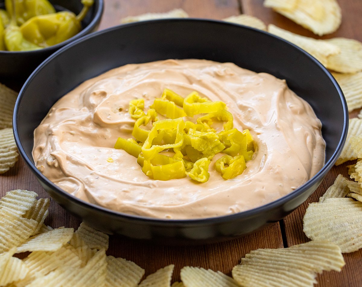 Black bowl filled with Mississippi Pot Roast Dip on a wooden table with potato chips around it.