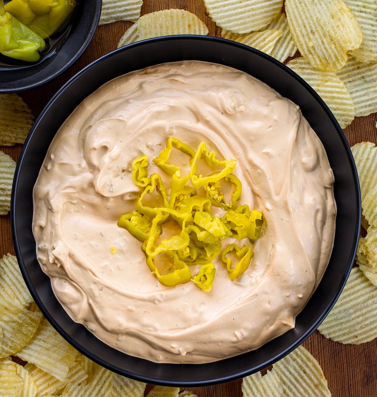 Black bowl filled with Mississippi Pot Roast Dip on a wooden table with potato chips around it from overhead.