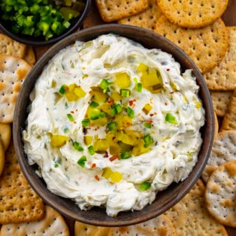 Bowl of Spicy Dill Pickle Dip surrounded by crackers on a wooden table from overhead.