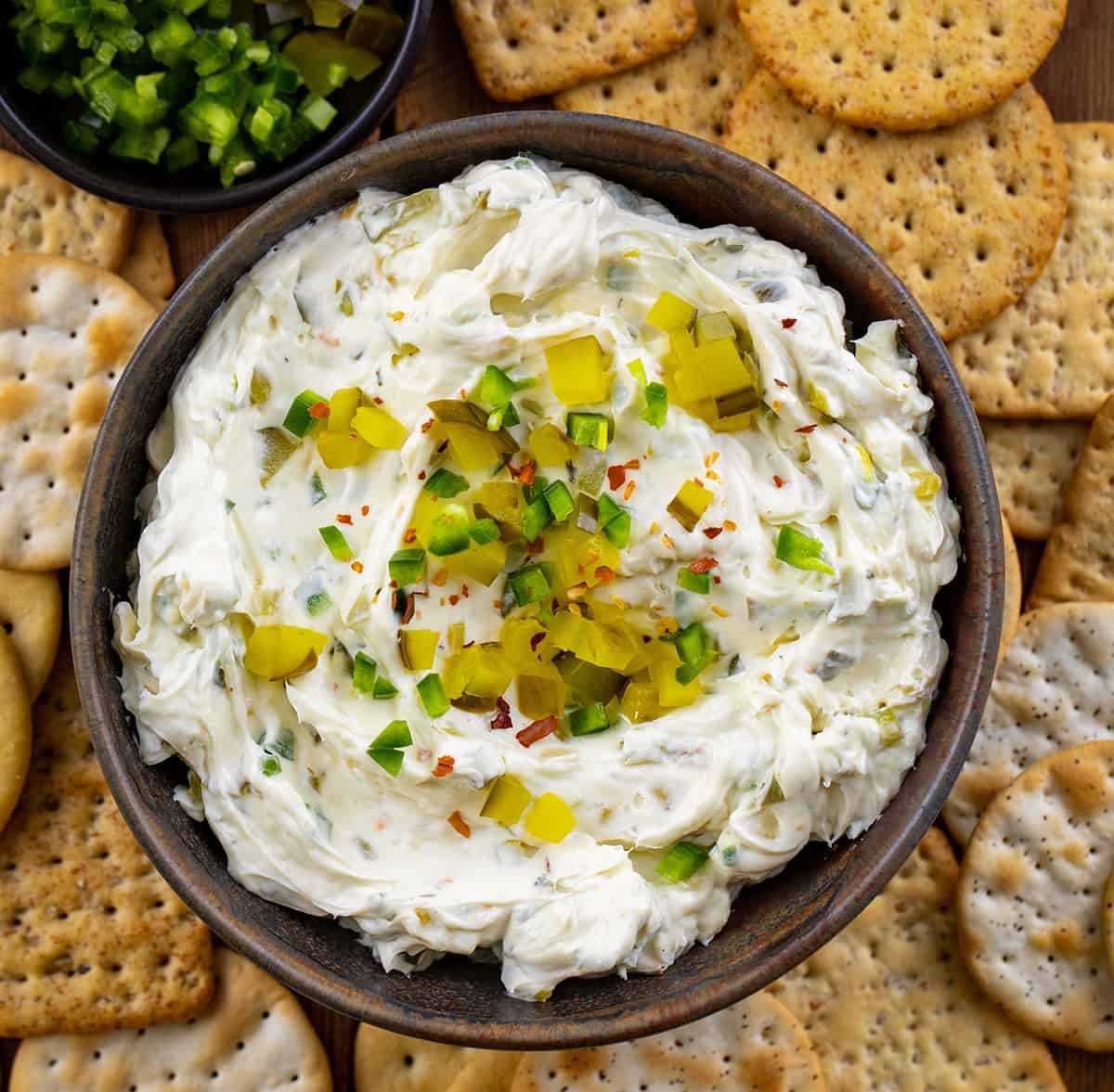 Bowl of Spicy Dill Pickle Dip surrounded by crackers on a wooden table from overhead.