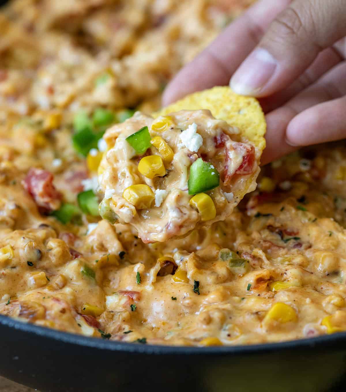 Hand holding a chip with Street Corn Queso.
