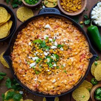 Street Corn Queso in a skillet on a wooden table surrounded with chips and roasted corn from overhead.